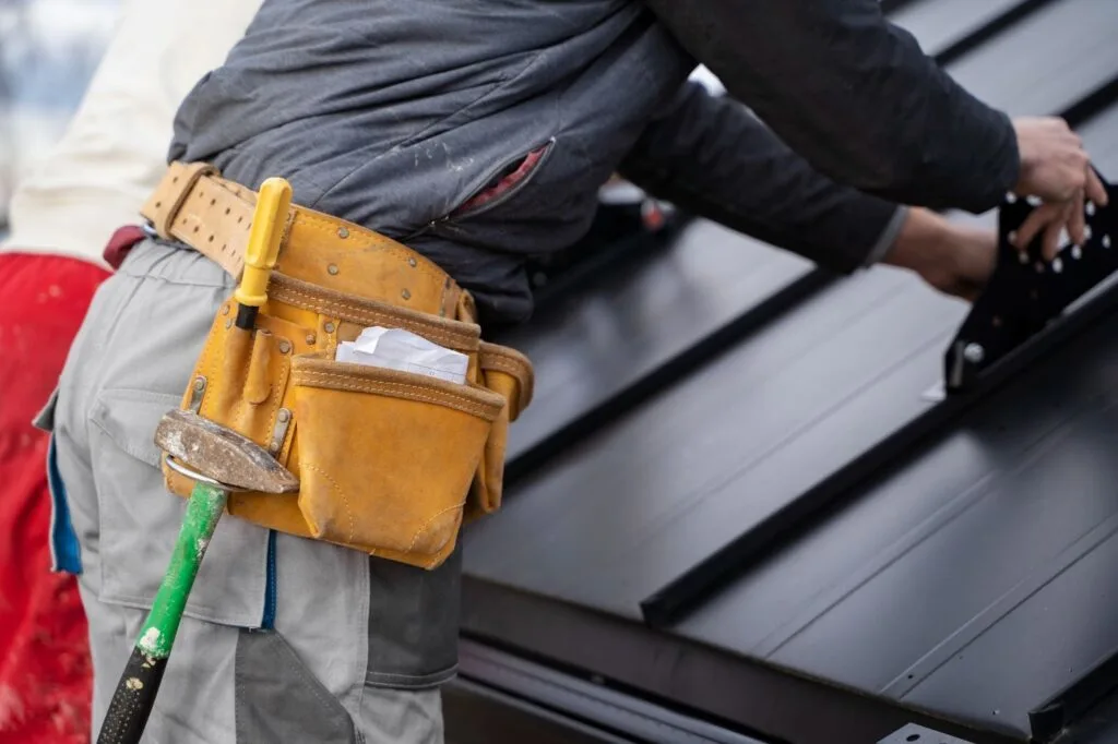 Close-up of a leather tool belt with a hammer worn by a metal roofing worker.