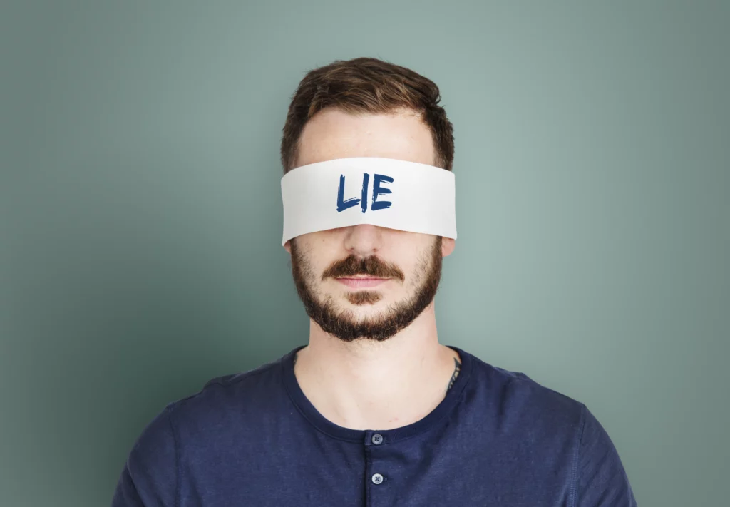 Bearded man wearing a white blindfold with the word LIE written on it.