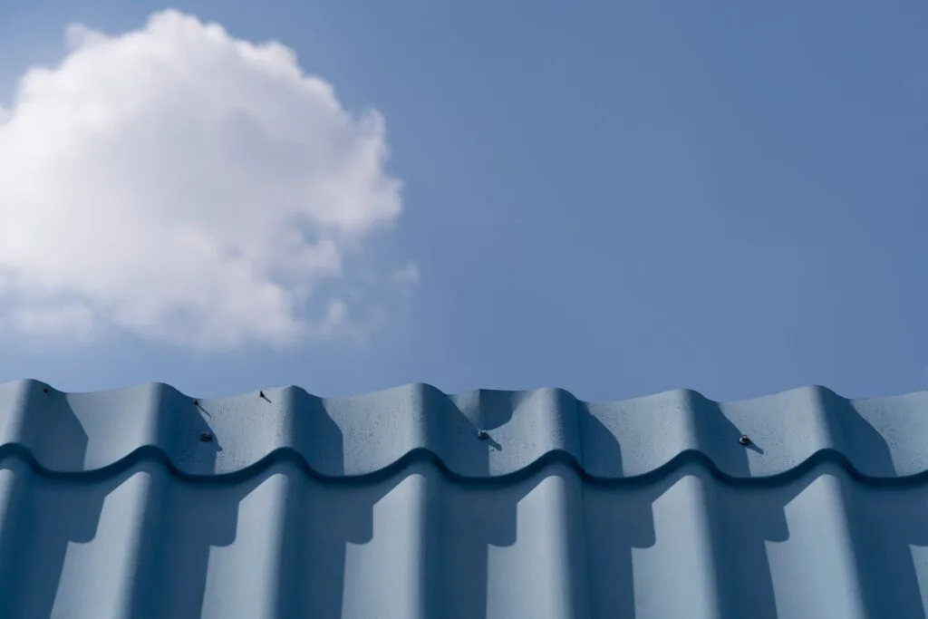 Blue corrugated roof under a clear blue sky with a white cloud.